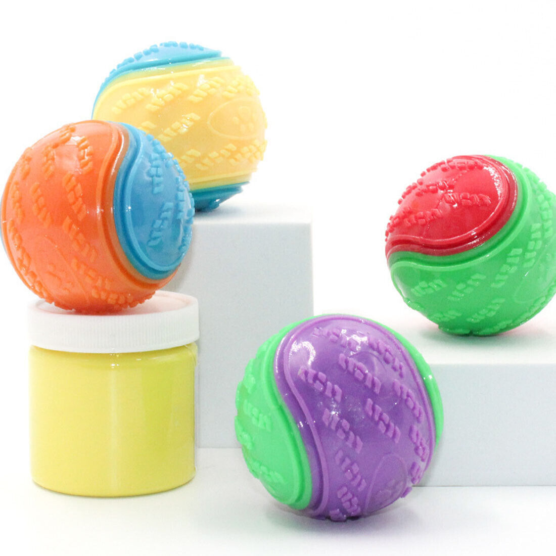 Colorful set of four squeaky dog balls in orange, yellow, red, and green displayed with a yellow container.